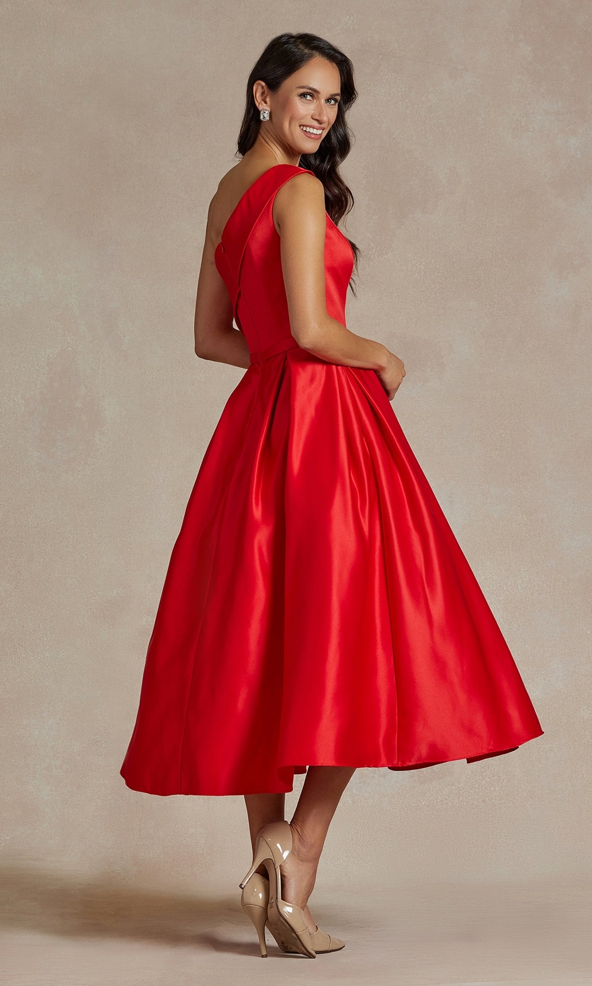 A woman wearing the One-Shoulder Simple Tea-Length Party Dress JE931 in vibrant red and beige high heels stands against a neutral background, looking over her shoulder and smiling.